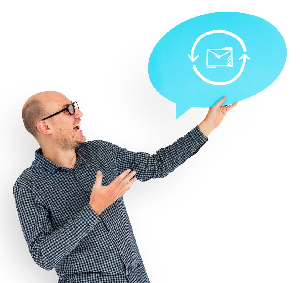 Man holding a dialogue balloon with mail icon Bald man with glasses smiling while holding a blue speech balloon with a mail icon, representing digital communication.