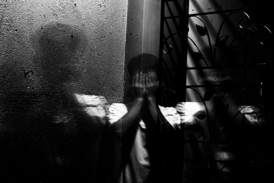 Shadow of a person with his hands on his face Black and white image of a person with his hands on his face and a shadow reflected on the wall, symbolizing anxiety, depression or internal struggle.