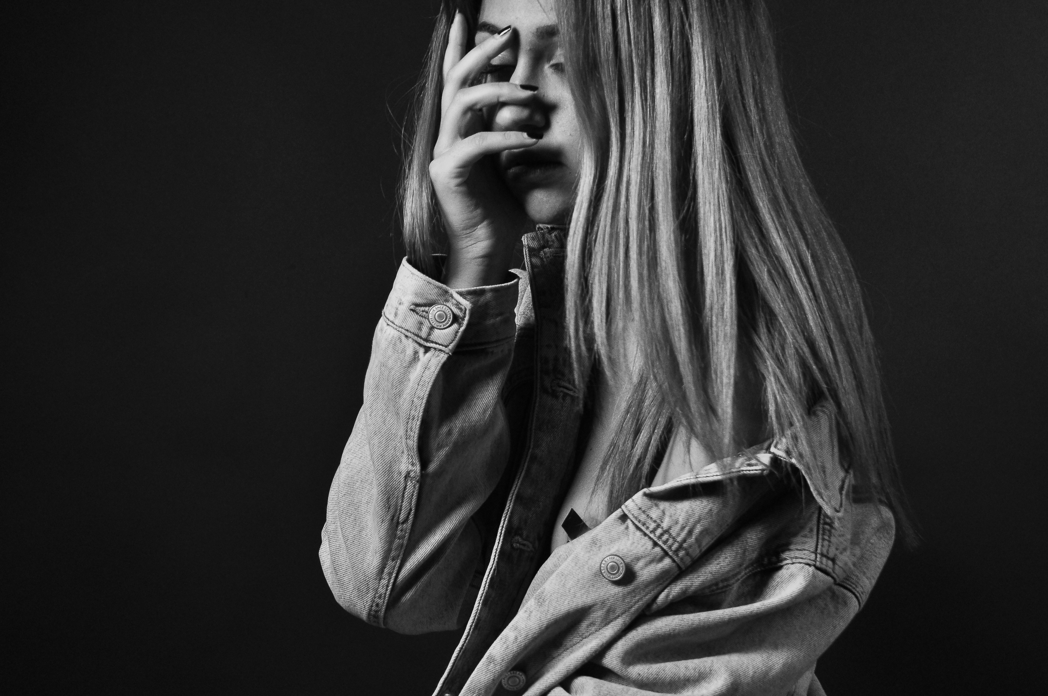 Woman in black and white with expression of anguish Black and white portrait of a woman in a denim jacket covering part of her face, reflecting anxiety, sadness or introspection.