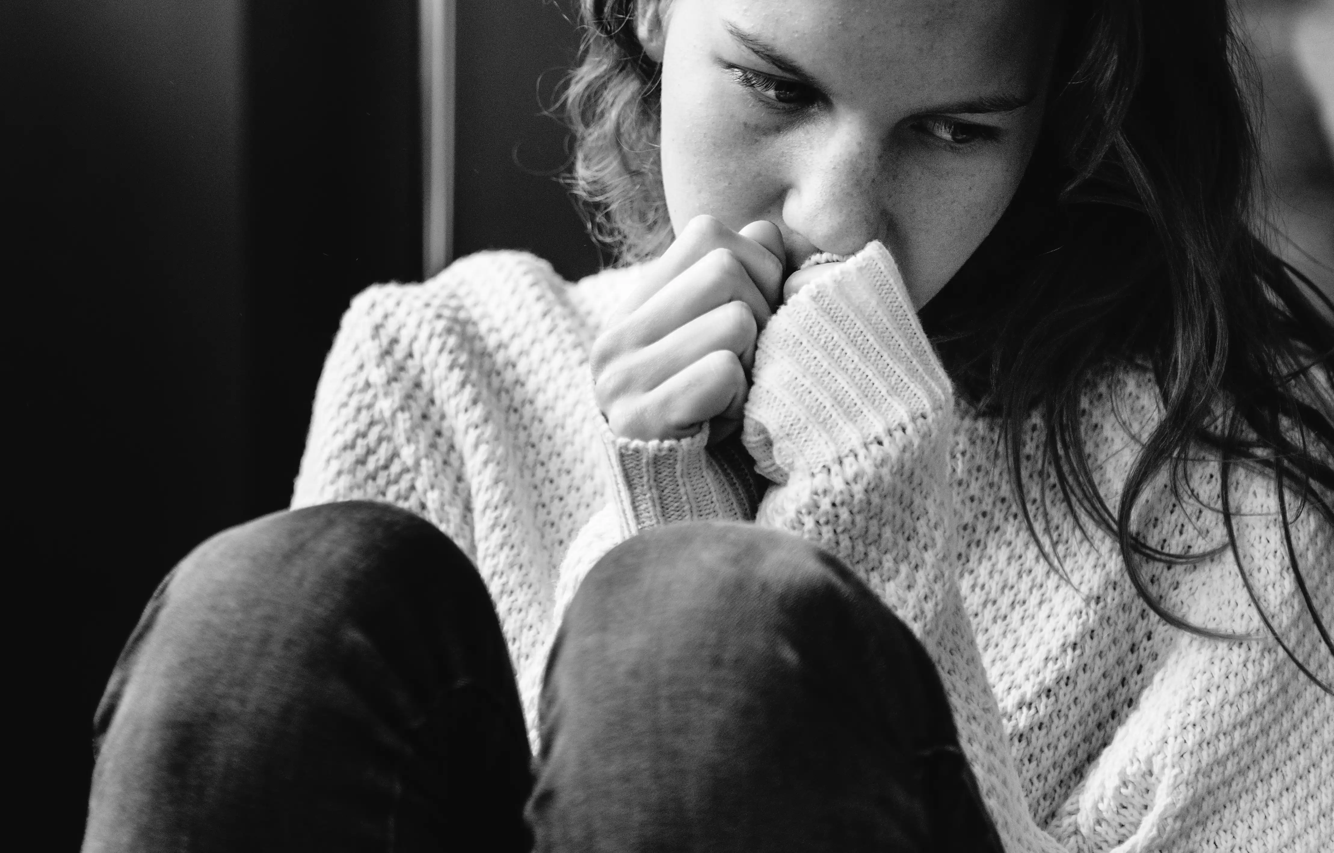 Sad woman in black and white Black and white portrait of a woman in a wool sweater, hugging herself with melancholic expression, reflecting sadness, anxiety or deep reflection.